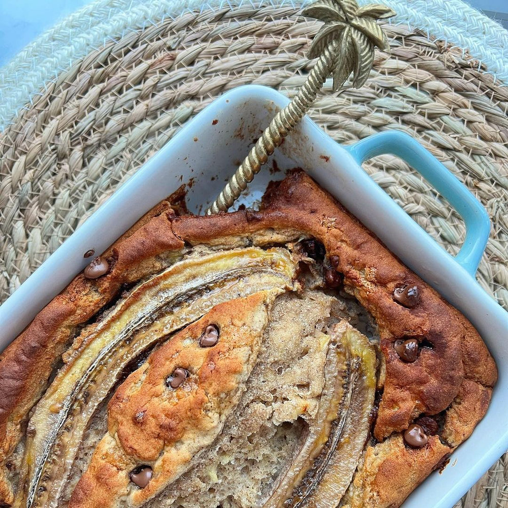 A rectangular dish with a chocolate chip cake and golden pineapple spoon inside