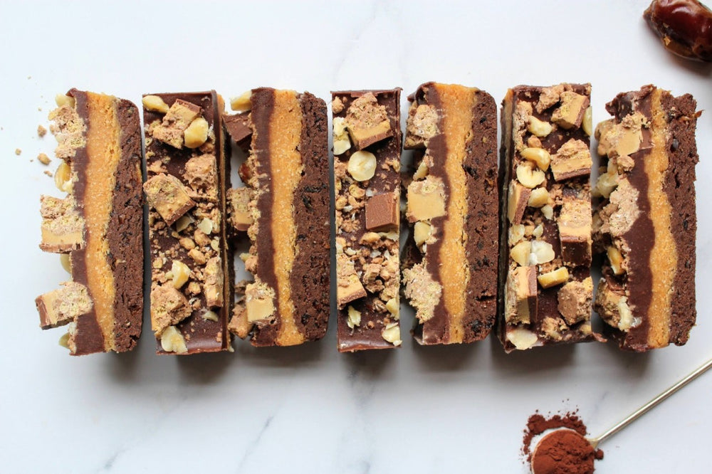 Millionaire's shortbread bars in a row topped with nuts and biscuit
