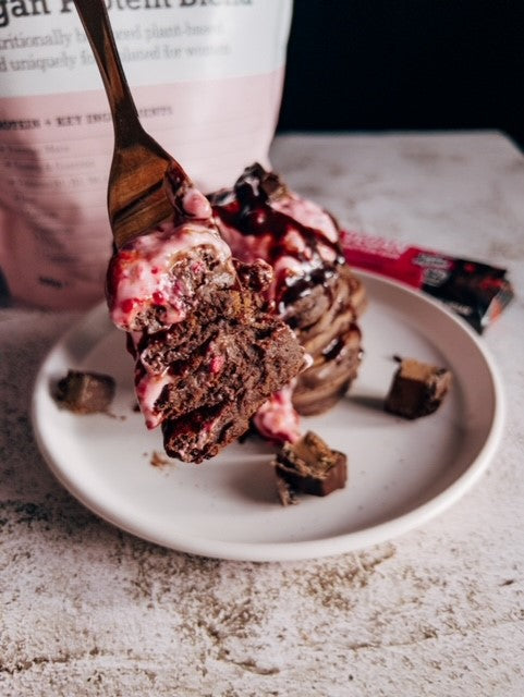 A stack of chocolate protein pancakes with strawberry frosting on top