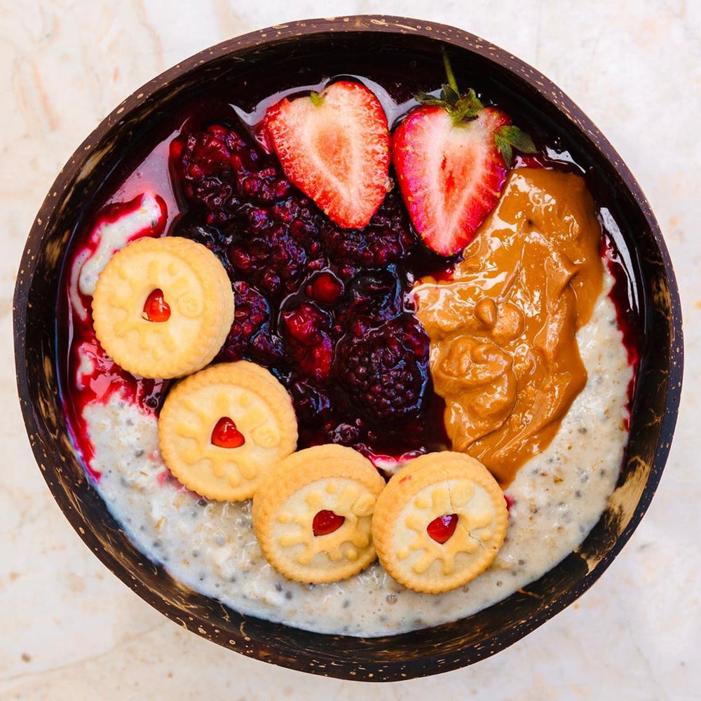 Close up of a protein smoothie bowl with jam, peanut butter, strawberries and biscuits