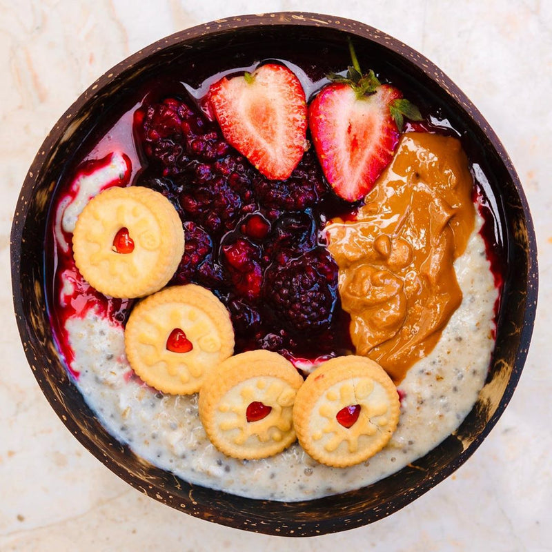 Close up of a protein smoothie bowl with jam, peanut butter, strawberries and biscuits